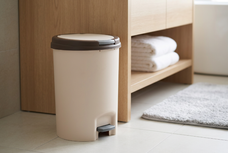 Covered trash can placed beside a bathroom vanity cabinet.